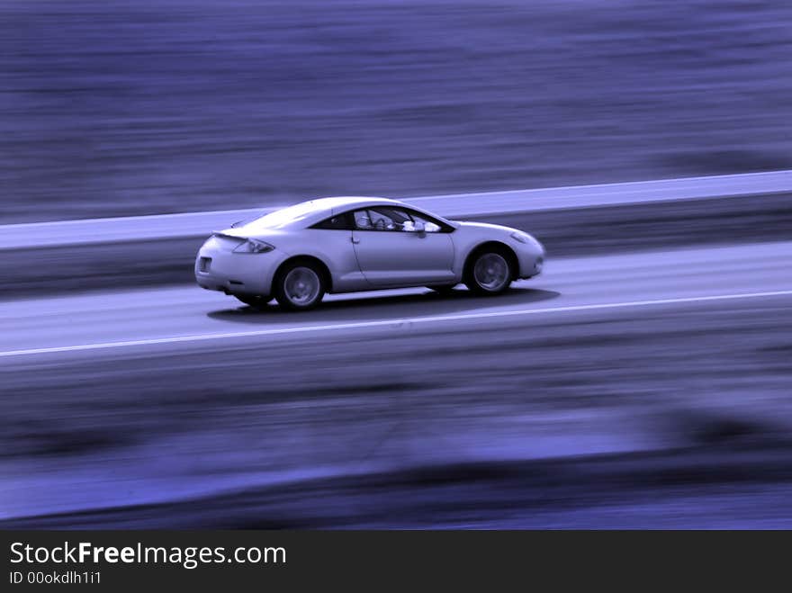 Two door sedan driving along road with blurred background