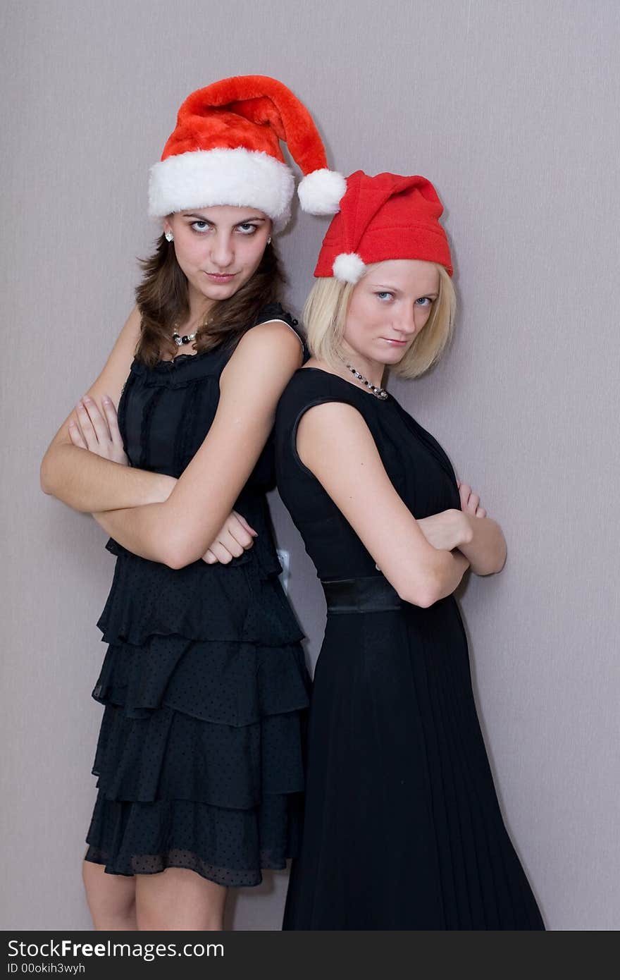 Two beautiful girls in red christmas caps and in black clothes threateningly look in a lens