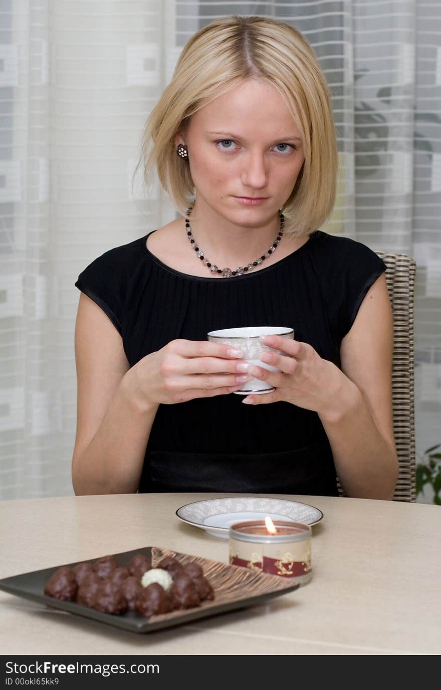 A beautiful woman in black clothes at the table has coffee