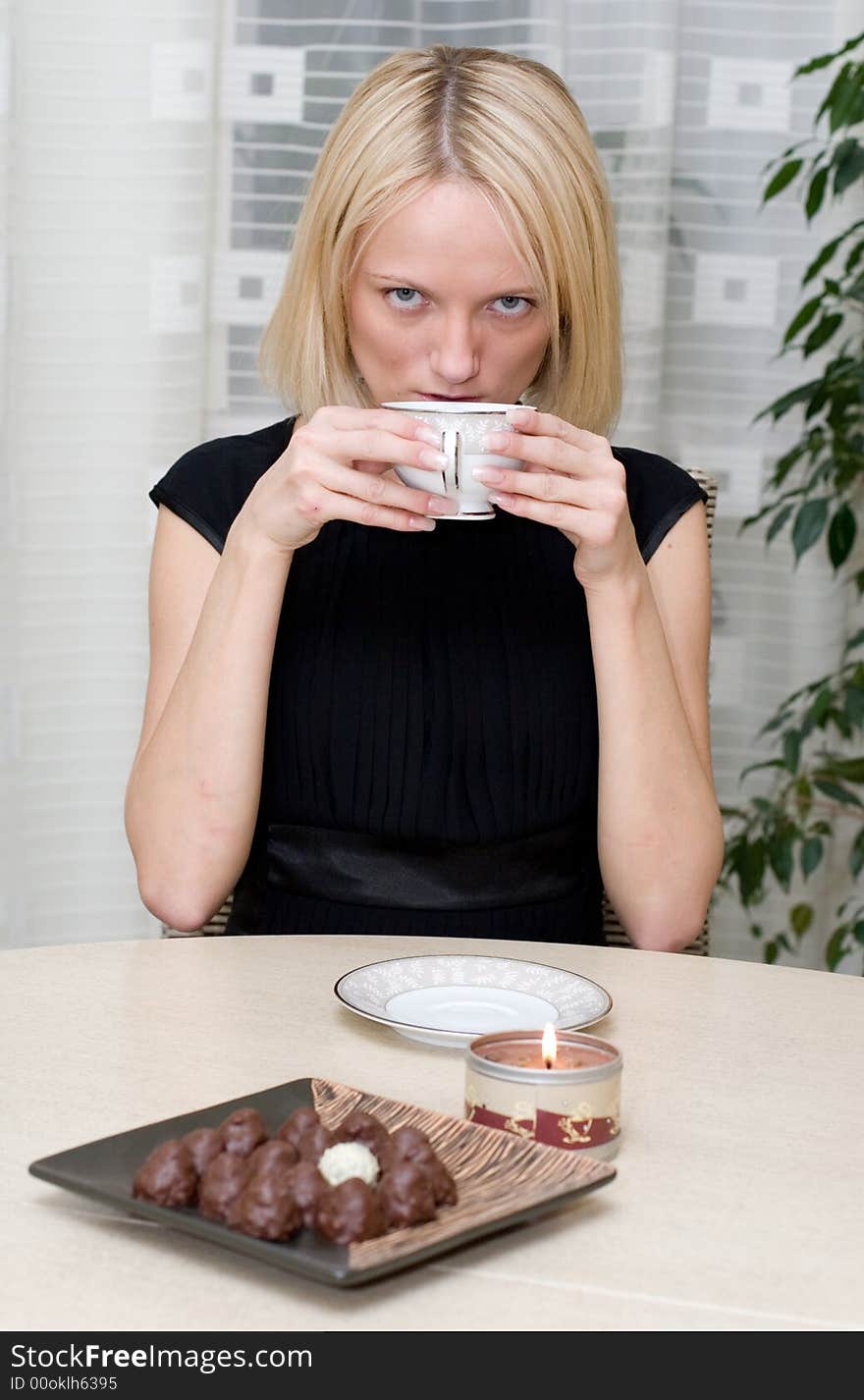 A beautiful woman in black clothes at the table has coffee