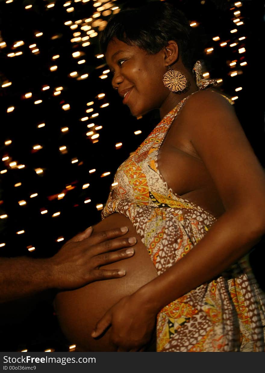 A hand of african american man touching his wife's belly with night bulbs setting on the background. the camera was moved to create moving background lights but the main subject was in focus. A hand of african american man touching his wife's belly with night bulbs setting on the background. the camera was moved to create moving background lights but the main subject was in focus