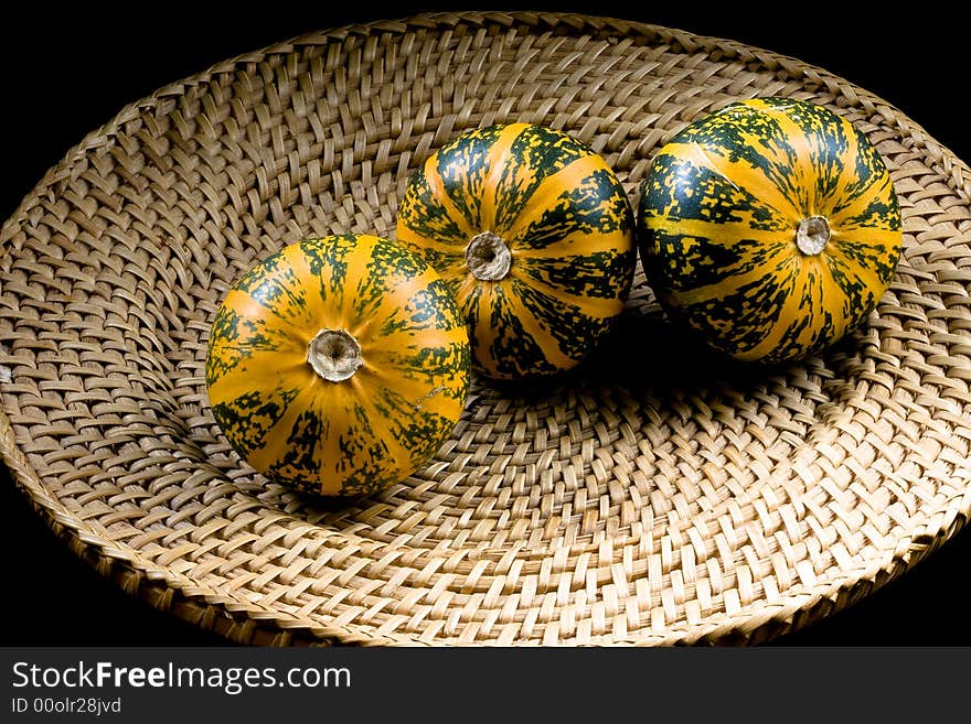 Three dark green-orange striped pumpkins placed on wickerwork plate. Three dark green-orange striped pumpkins placed on wickerwork plate