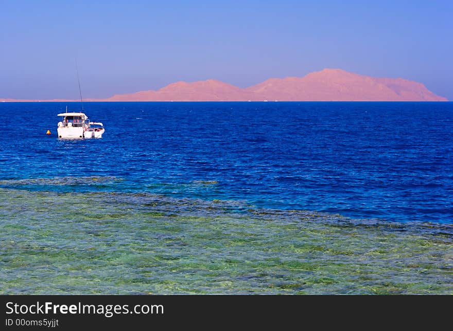 Rocky island in the sea with white boat