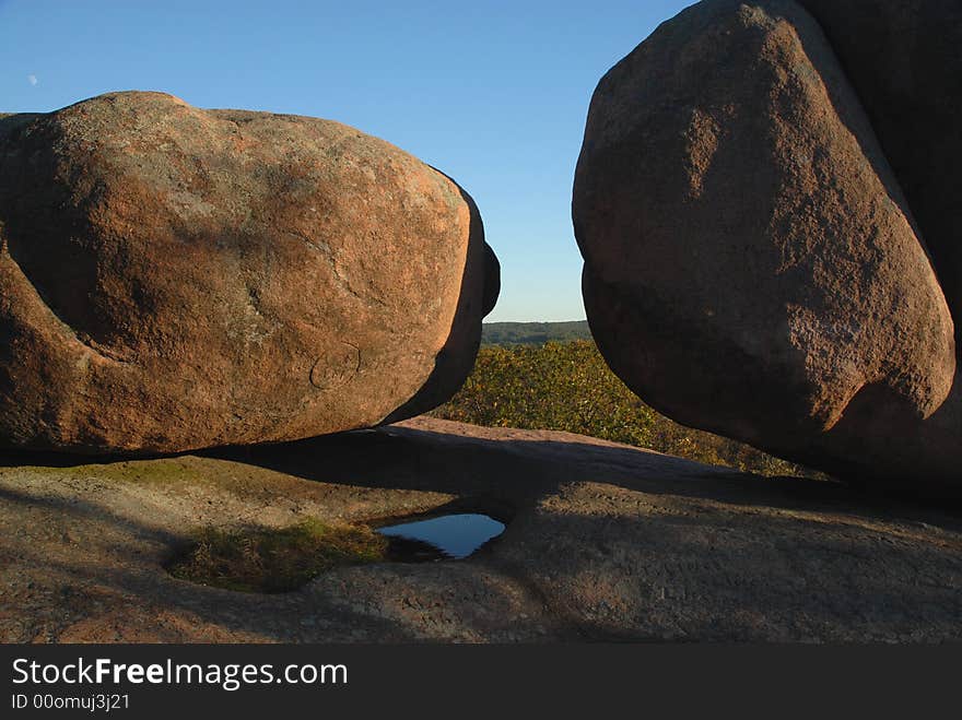 Two boulders with blue sky and the moon in the background.