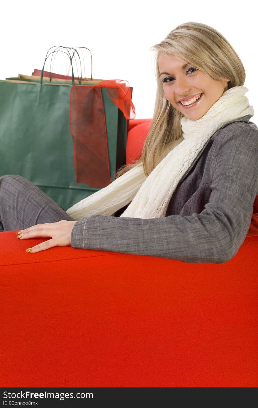 Young, happy woman sitting on couch with shopping bags. Looking at camera, side view. White background.