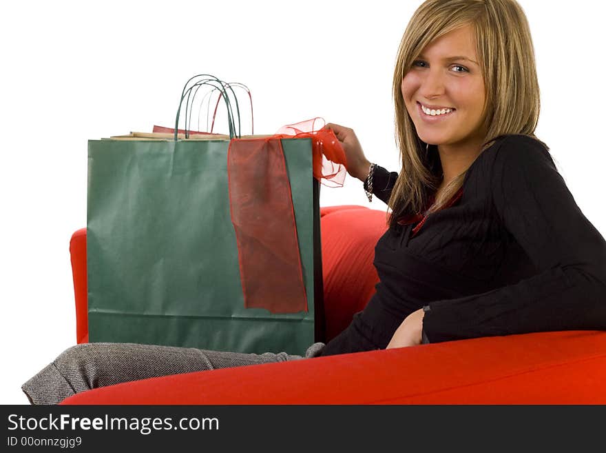 Young, happy woman sitting on couch with shopping bags. Looking at camera, side view. White background. Young, happy woman sitting on couch with shopping bags. Looking at camera, side view. White background.