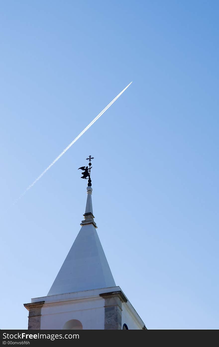 Belfry tower with an angel weather vane pointing to the sky cruise by a jet plane. Belfry tower with an angel weather vane pointing to the sky cruise by a jet plane