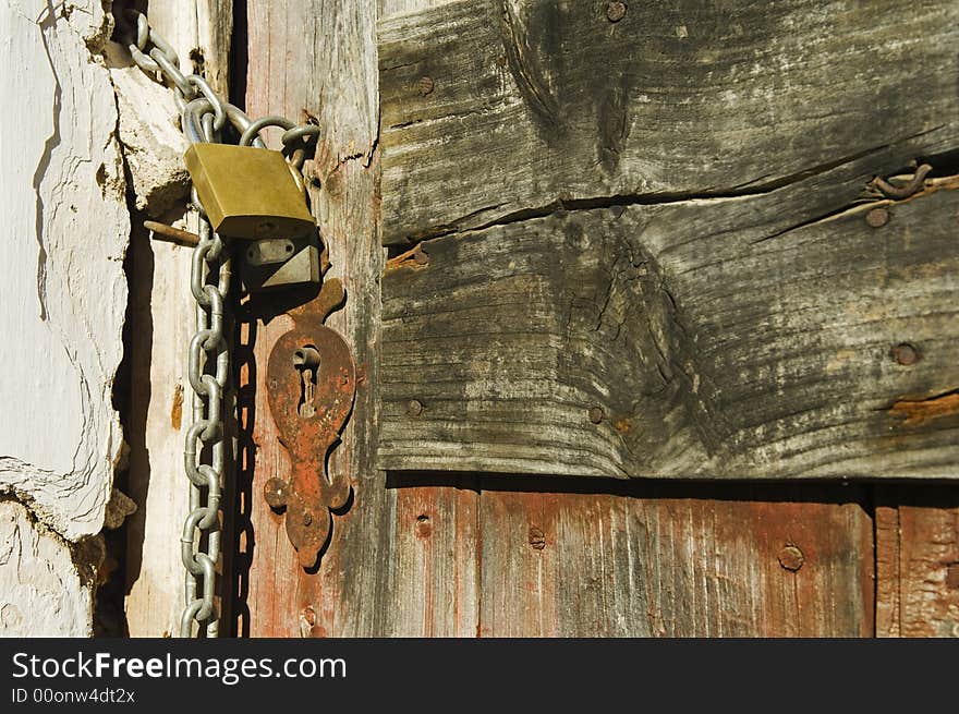 Old drab door secured with a padlock and iron chain. Old drab door secured with a padlock and iron chain.