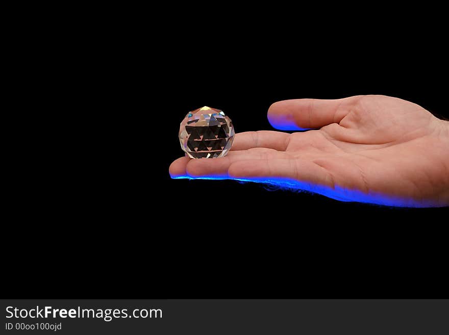 Multi faceted crystal globe sitting on finger tips of a man lit from below with blue theatrical lighting against a black background. Multi faceted crystal globe sitting on finger tips of a man lit from below with blue theatrical lighting against a black background