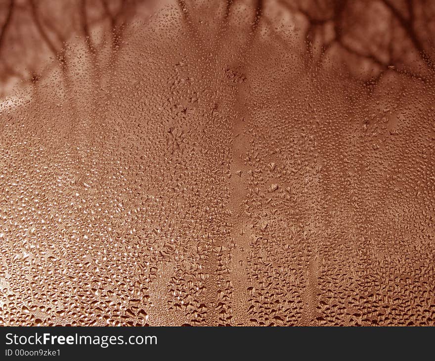 Close-up clear drops of water on window glass surface with tree branches at a distance. Close-up clear drops of water on window glass surface with tree branches at a distance