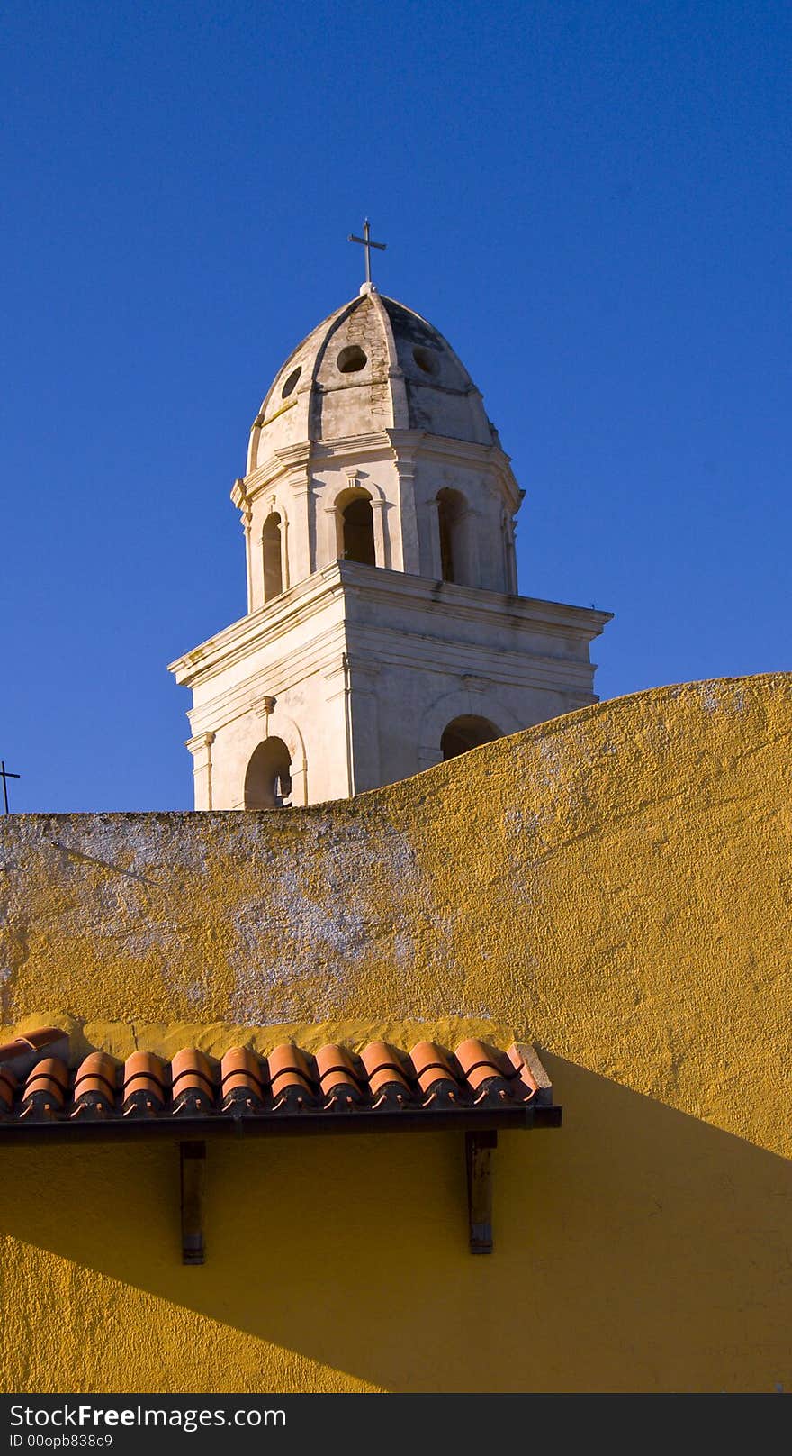 View of a bell tower against a blue sky with a yellow wall in foreground. View of a bell tower against a blue sky with a yellow wall in foreground