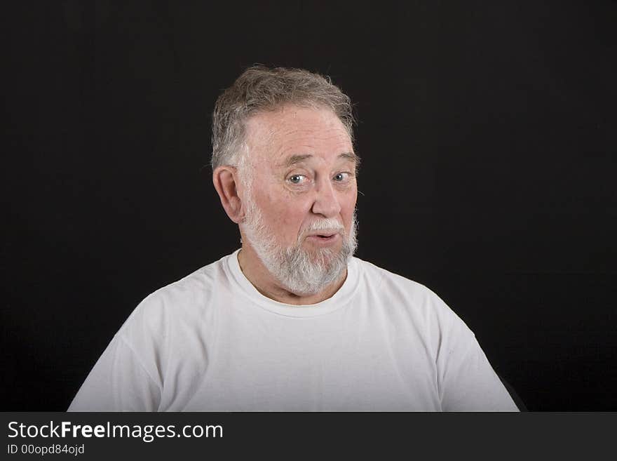 A senior man in white tshirt on black background with a very expressive face. A senior man in white tshirt on black background with a very expressive face