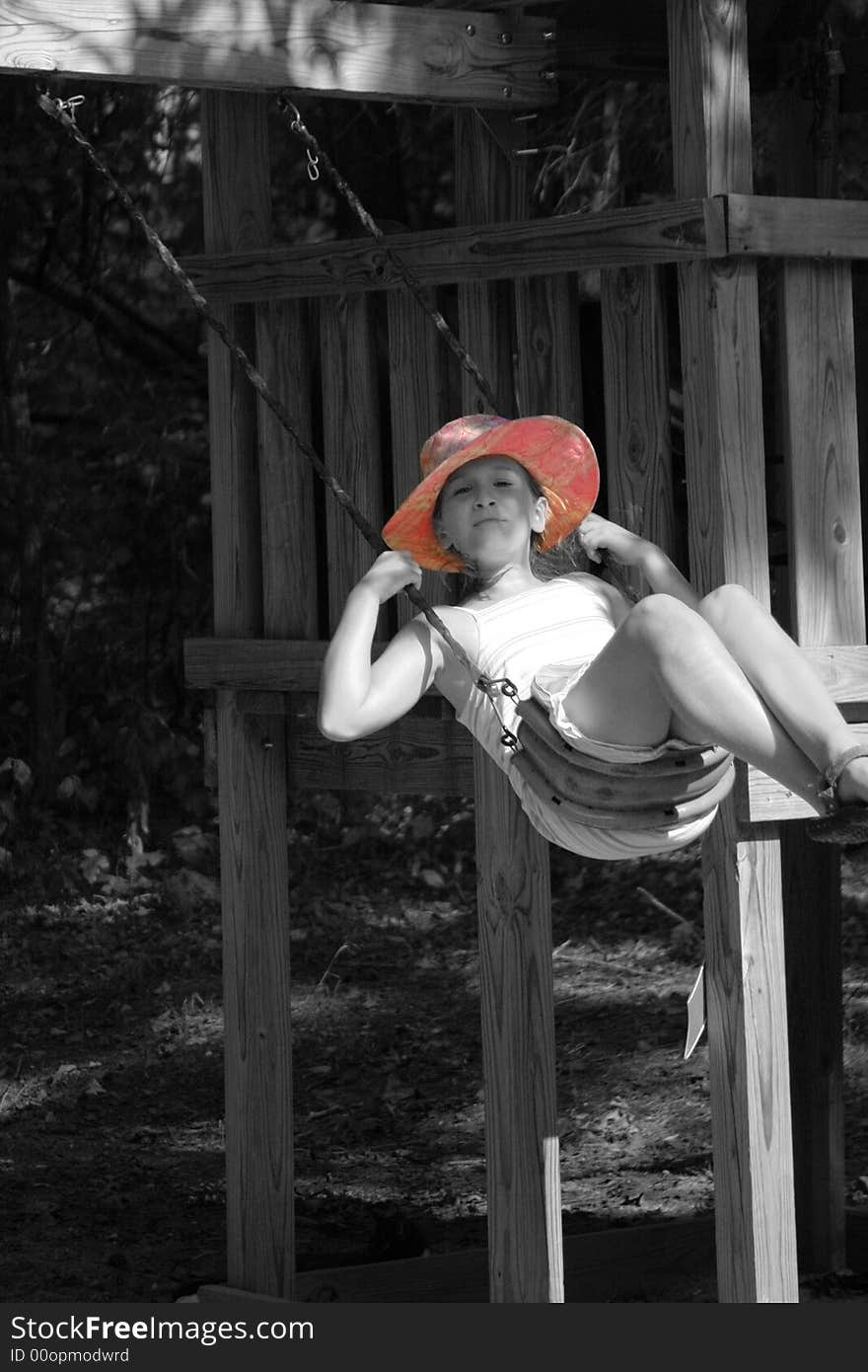 A young girl swings on a swingset with a pink summer hat and selective saturation