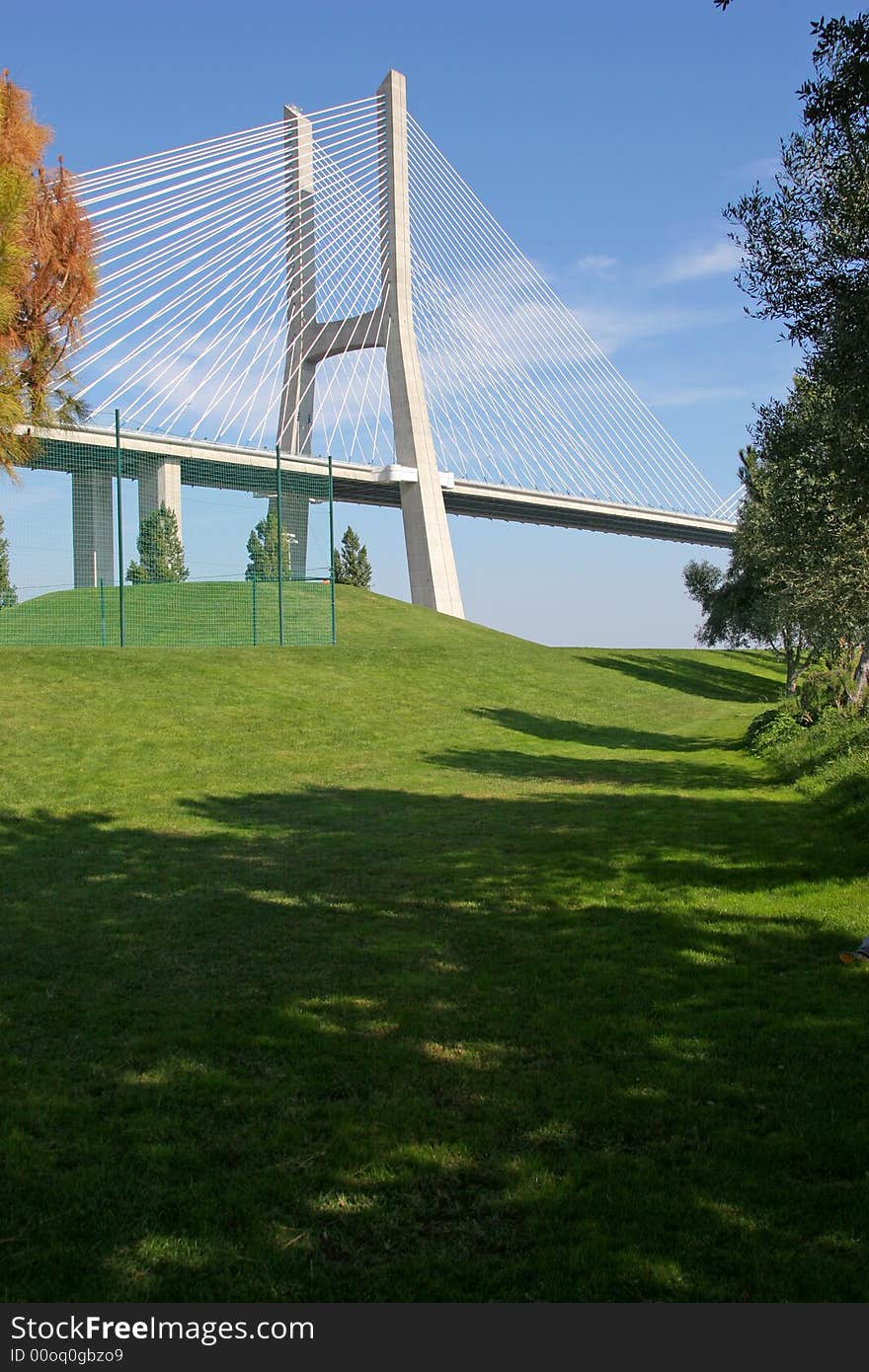 View of one of Lisbon's bridges with a grass lawn and trees in foreground. View of one of Lisbon's bridges with a grass lawn and trees in foreground