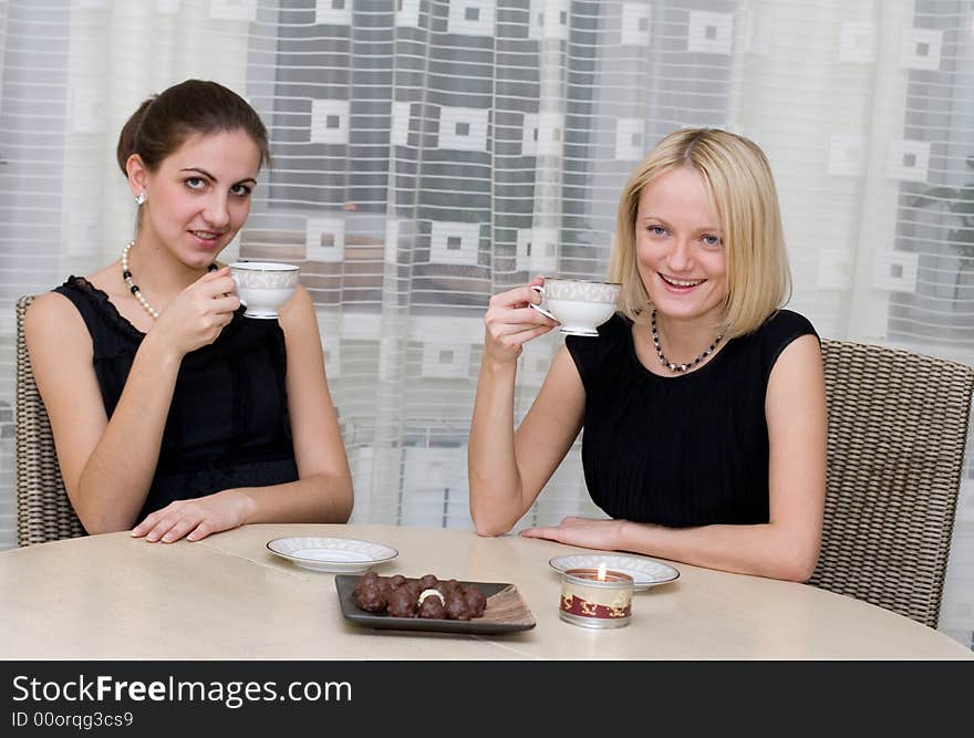 Two smiling girls have coffee with candy