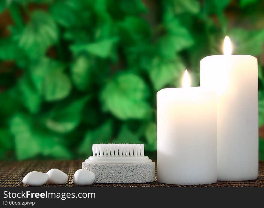 Two white candles,a pumice and a few white stones before green leaf. Two white candles,a pumice and a few white stones before green leaf