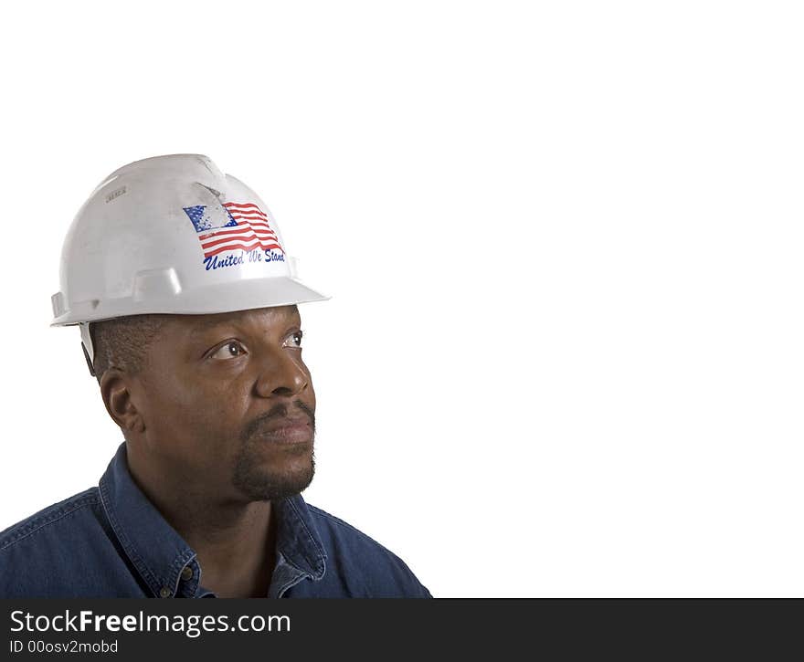 A black construction worker in blue denim shirt and white hard hat looking up into copy space. A black construction worker in blue denim shirt and white hard hat looking up into copy space