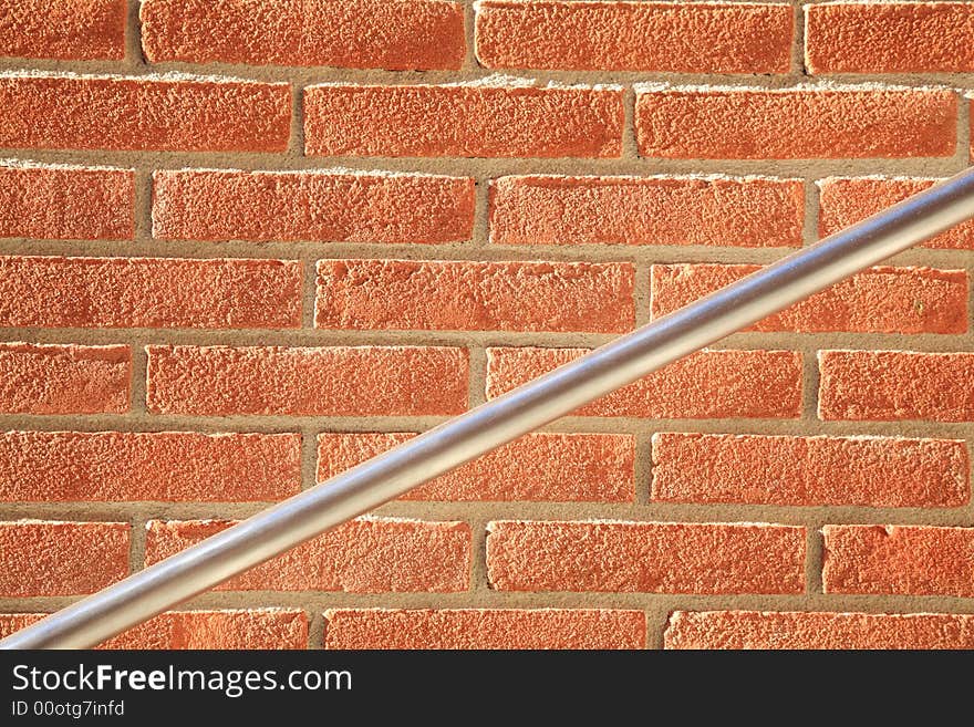 Photo of a plain red brick wall texture with diagonal metal handrail. Photo of a plain red brick wall texture with diagonal metal handrail