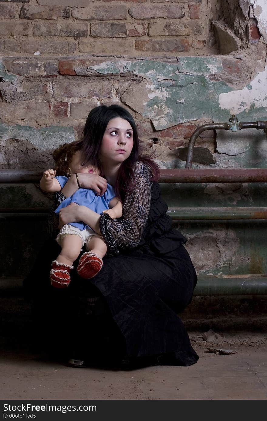 The girl in dark clothes with a doll scaredly looks. The girl in dark clothes with a doll scaredly looks