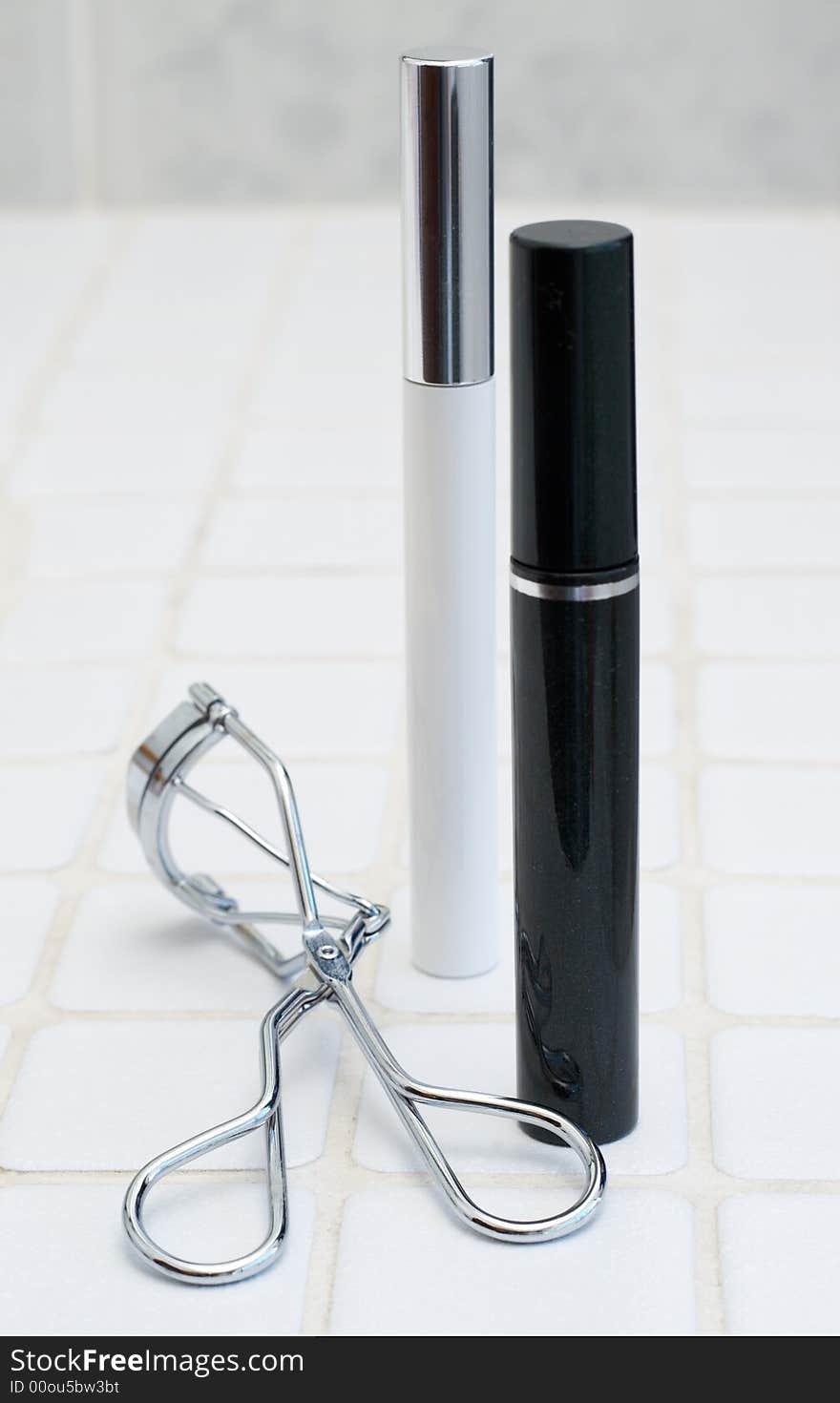 A set of black mascara and white lash treatment with silver lash curling tongs. A set of black mascara and white lash treatment with silver lash curling tongs