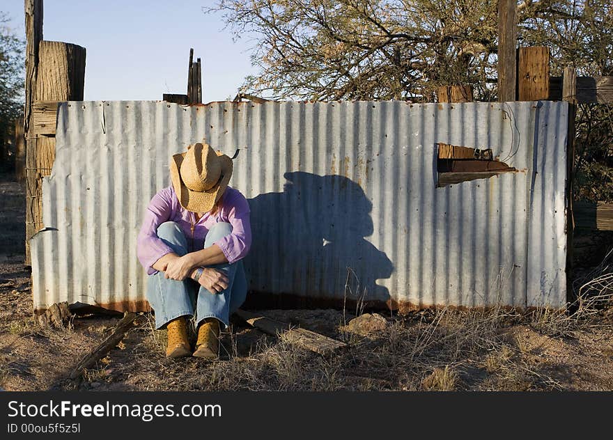 Woman wearing a straw cowboy hat with her head down leaning against a corrugated metal fence. Woman wearing a straw cowboy hat with her head down leaning against a corrugated metal fence.