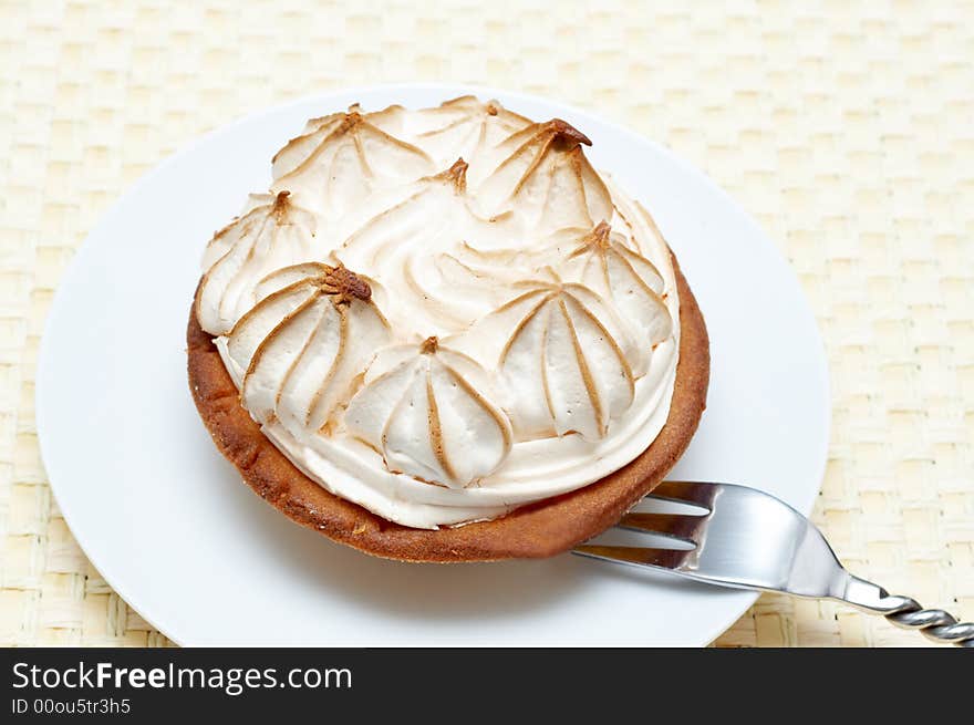 Miniature lemon meringue cake with small silver fork shot on a light wooden background