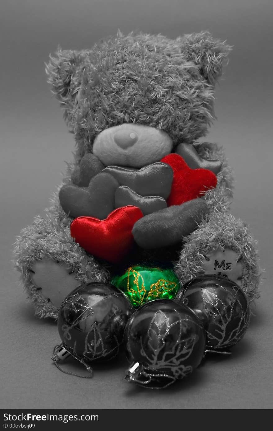 A teddy bear holding hearts in his hands with christmas balls in front. A teddy bear holding hearts in his hands with christmas balls in front.