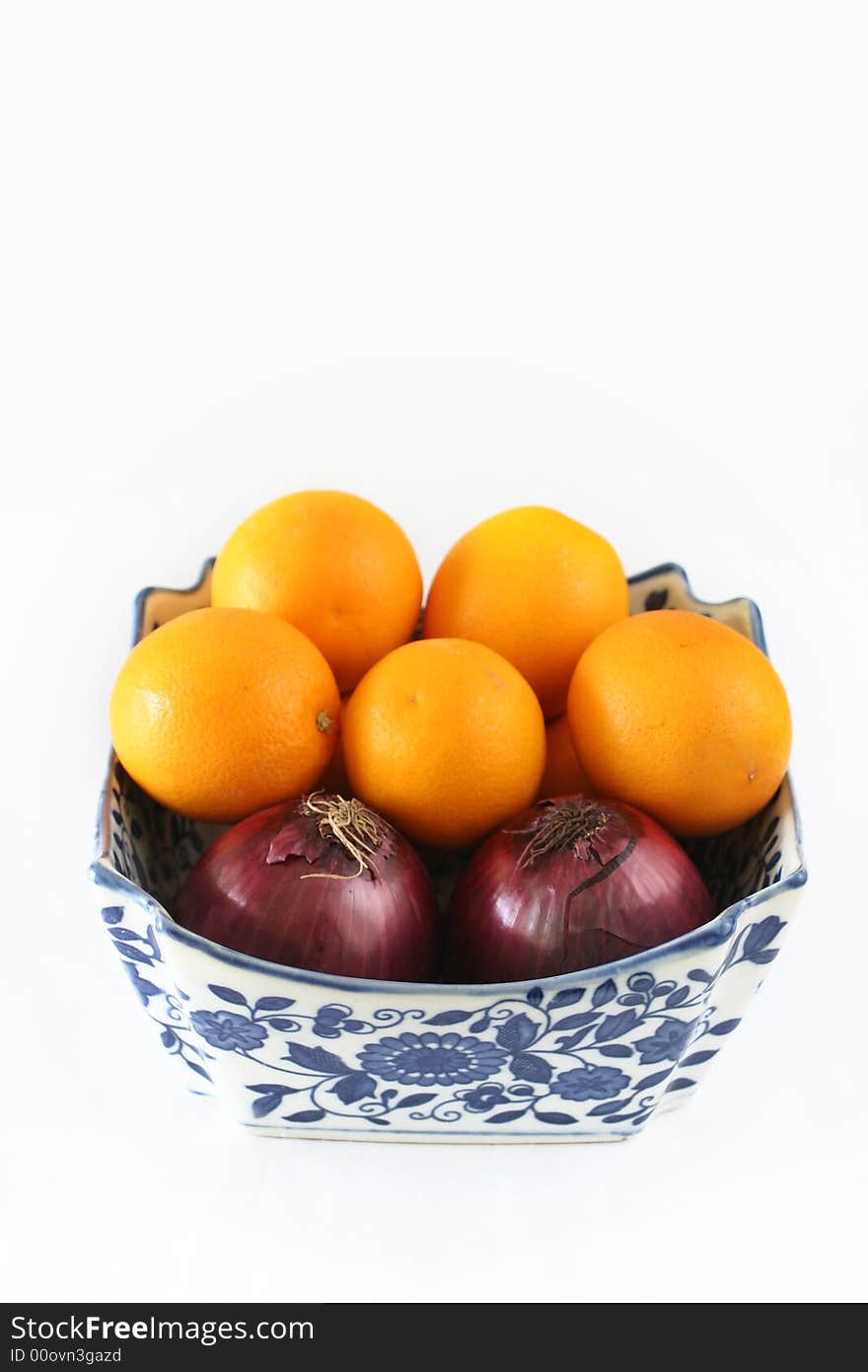 Organic onions and oranges in a square, ornate china cowl. Organic onions and oranges in a square, ornate china cowl