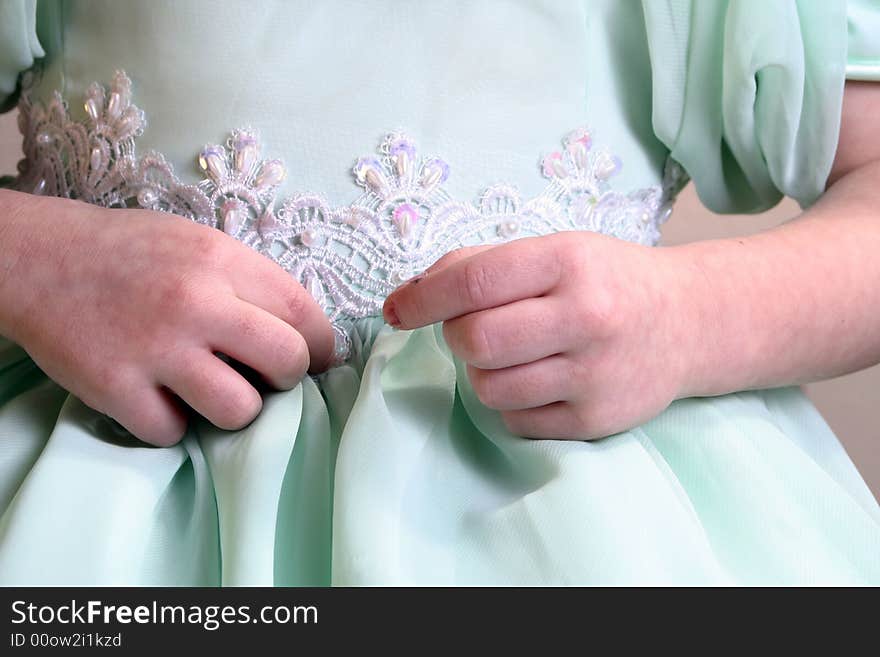 The tiny hands of a toddler pick at the lace on her dress. The tiny hands of a toddler pick at the lace on her dress