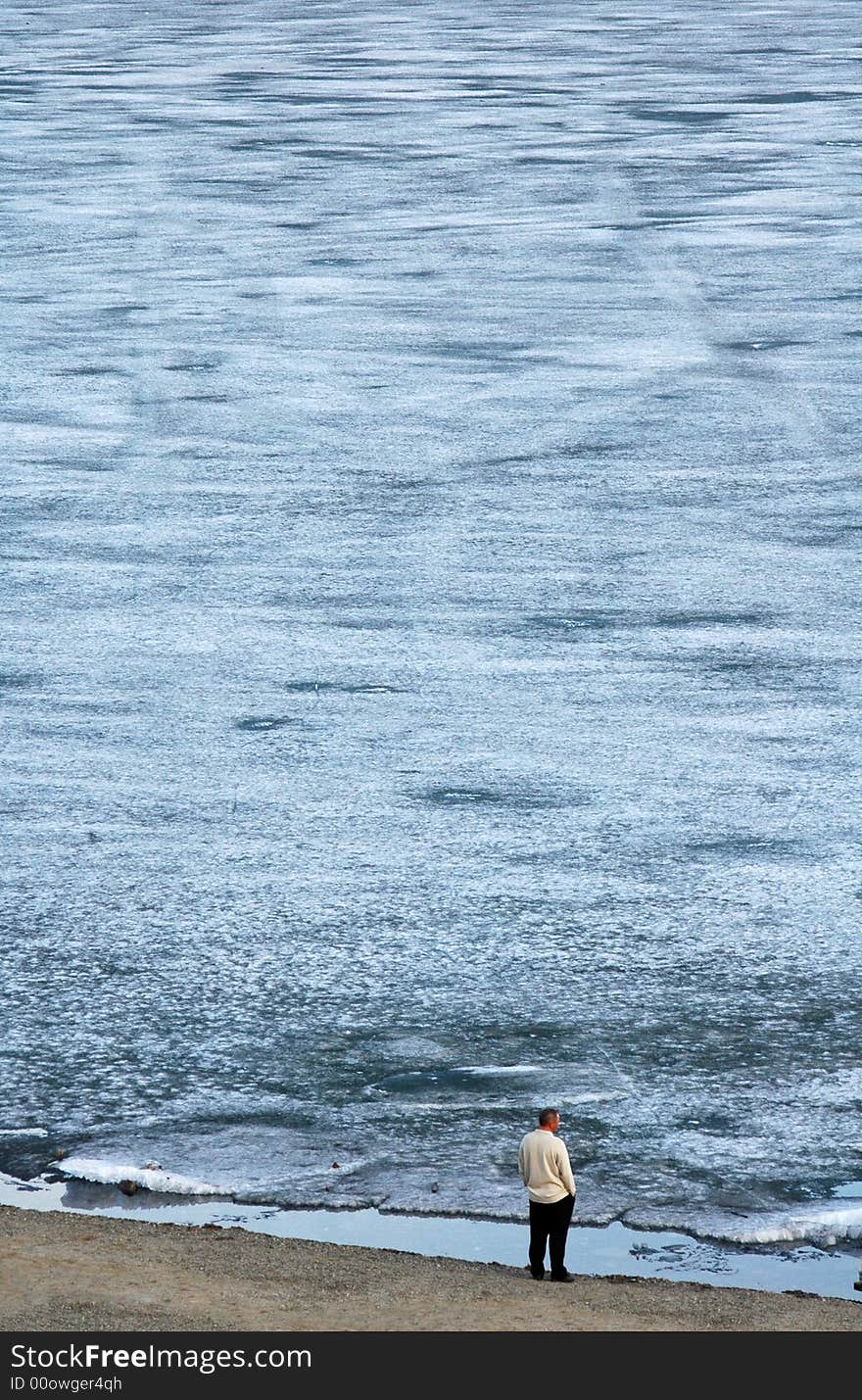 Lone man looking at the frozen water, standing on the shore. Lone man looking at the frozen water, standing on the shore