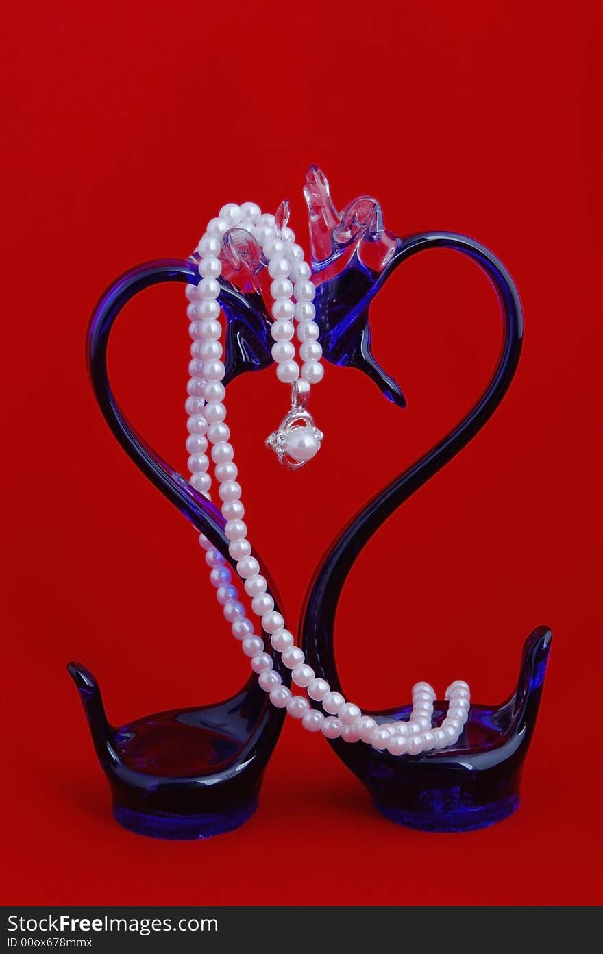 Glass blue swans surrounded with a pearl beads on red. Glass blue swans surrounded with a pearl beads on red