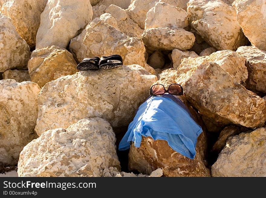 Sunglasses, sandals, and shirt laying on the rocks by the ocean. Sunglasses, sandals, and shirt laying on the rocks by the ocean