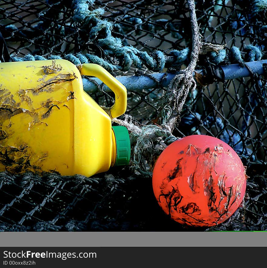 A fishing net on whitch there is a red buoy, an old empty yellow drum and blue moorings