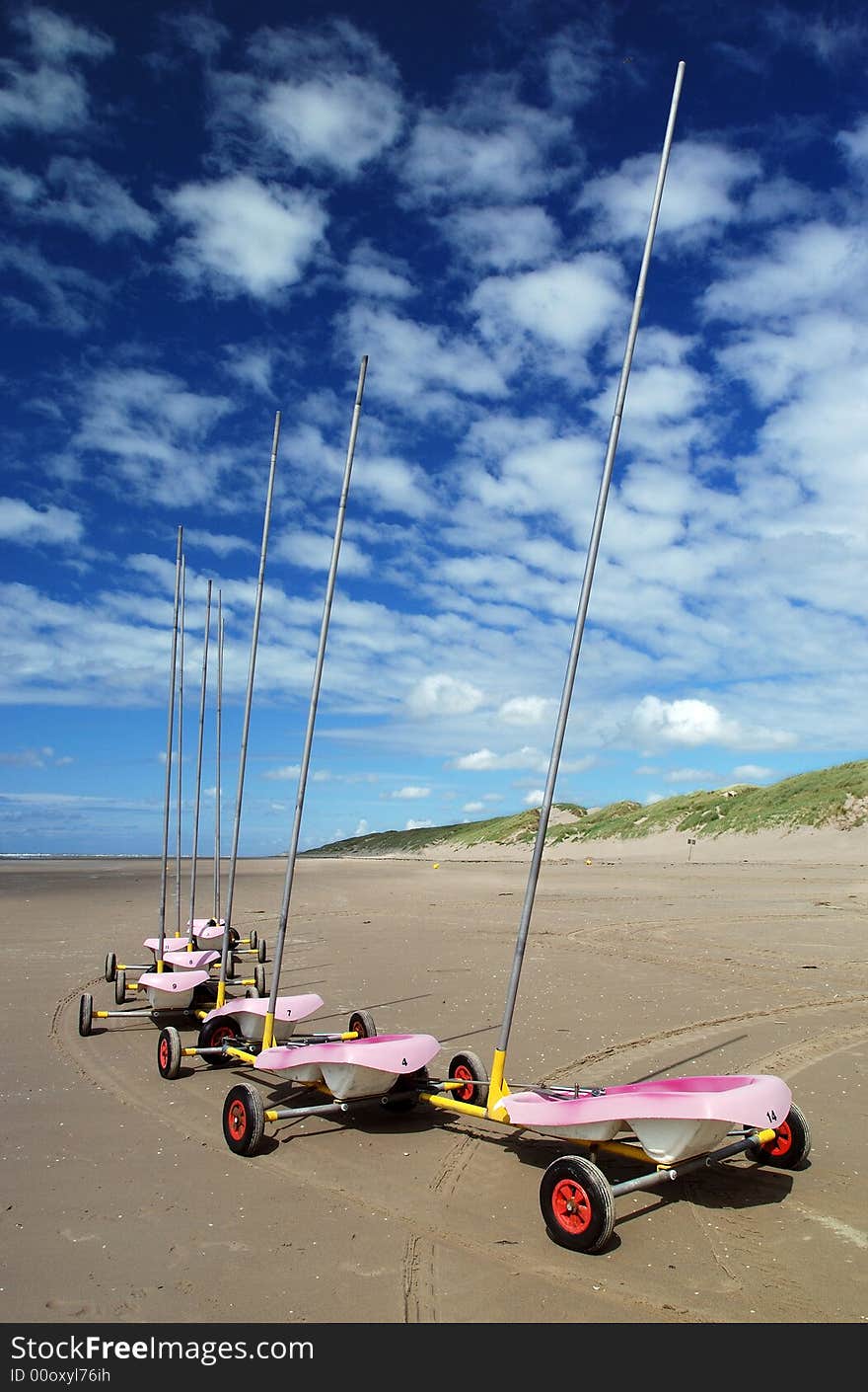 Pink land sand yachts in a single file on the beach under blue sky and lovely clouds. Pink land sand yachts in a single file on the beach under blue sky and lovely clouds