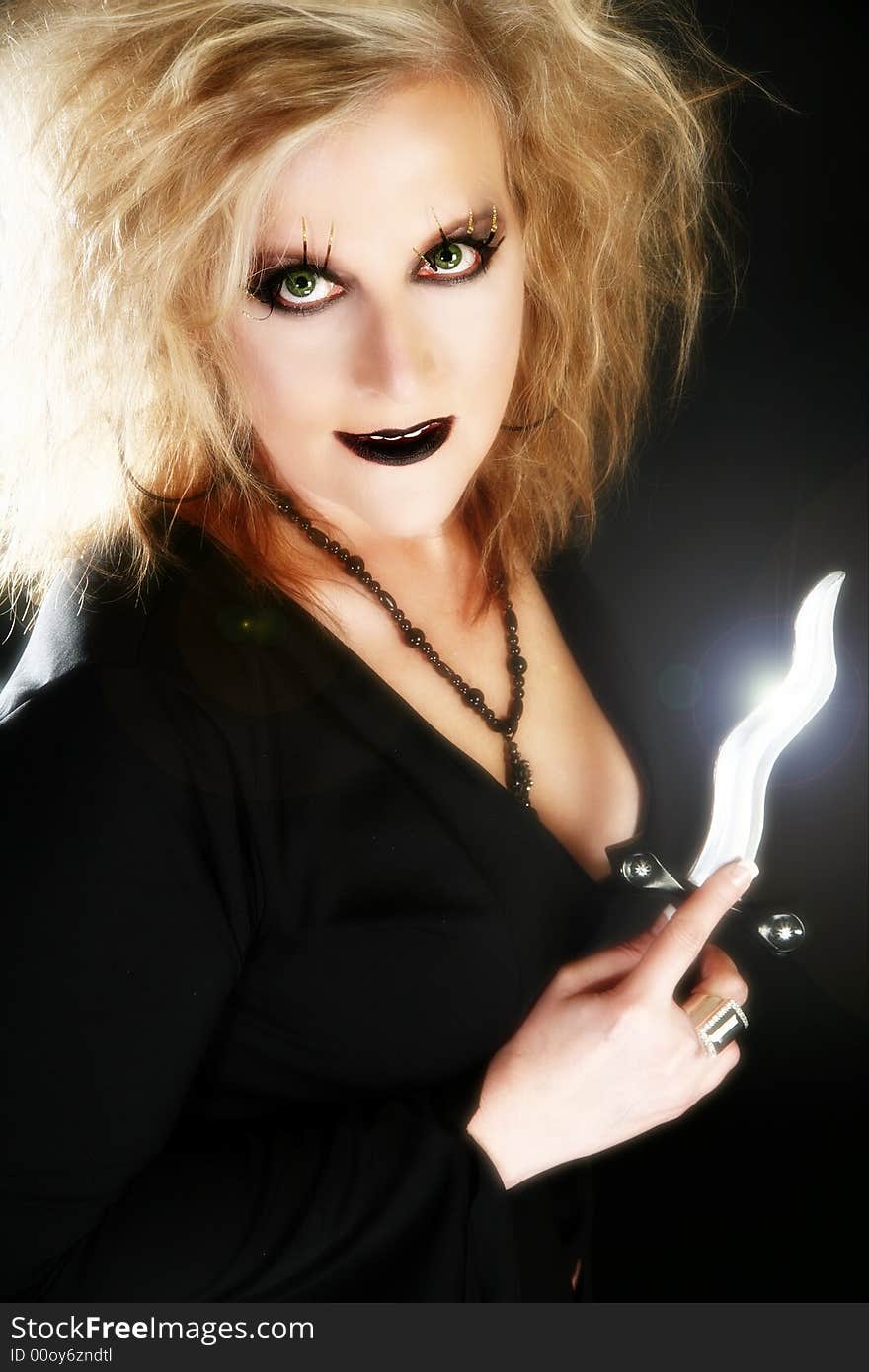 Beautiful 40 year old woman dressed as witch holding dagger over black background.