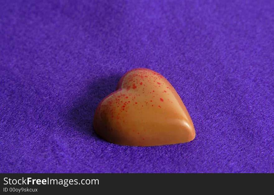 Heart shape chocolate with red dots over a silky violet background.