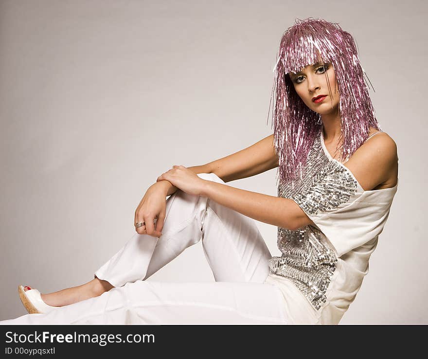 Beautiful girl dressed for carnival wearing glossy pink wig and silver blouse on light background. Beautiful girl dressed for carnival wearing glossy pink wig and silver blouse on light background