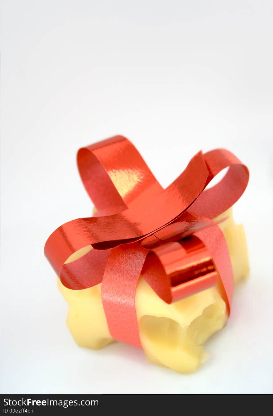 Cheese cube decorated as gift box. Cheese with big holes. It's decorated with red ribbons and bow on top and looks like a present. Shot over white paper (natural background). There is place for text above object. Cheese cube decorated as gift box. Cheese with big holes. It's decorated with red ribbons and bow on top and looks like a present. Shot over white paper (natural background). There is place for text above object.