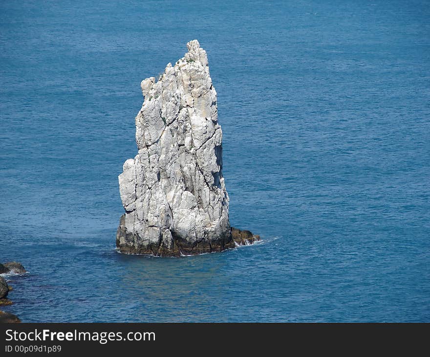 Lonely rock near a coast looks like a sailing-vessel