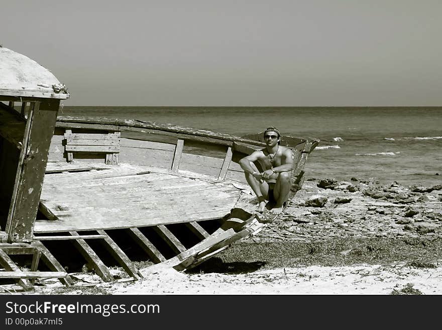 B/W portrait of a man sitting on the ship wreck on a beach. B/W portrait of a man sitting on the ship wreck on a beach.