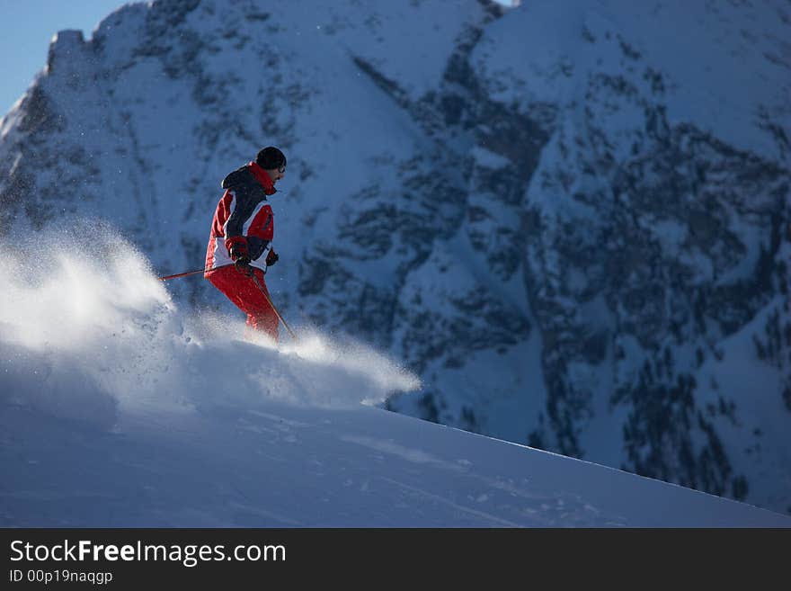 Powder skiing in front of huge mountain - selective focus lit from behind. Powder skiing in front of huge mountain - selective focus lit from behind