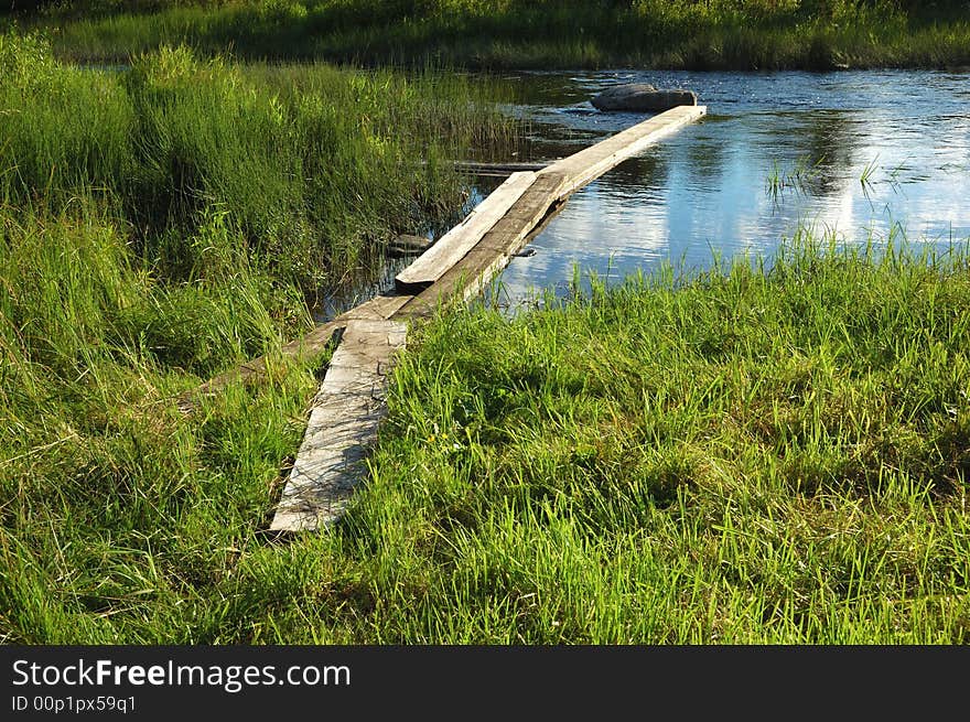 Planked footway across the creek, green grass around. Planked footway across the creek, green grass around