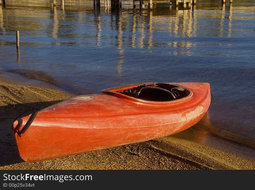 A red kayak half on the beach and half in the water ready to go.