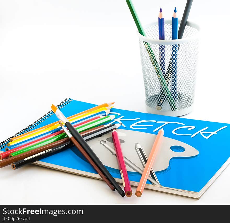 Still life of a sketch pad, color pencils, paintbrushes and a pencil holder on white background. Still life of a sketch pad, color pencils, paintbrushes and a pencil holder on white background