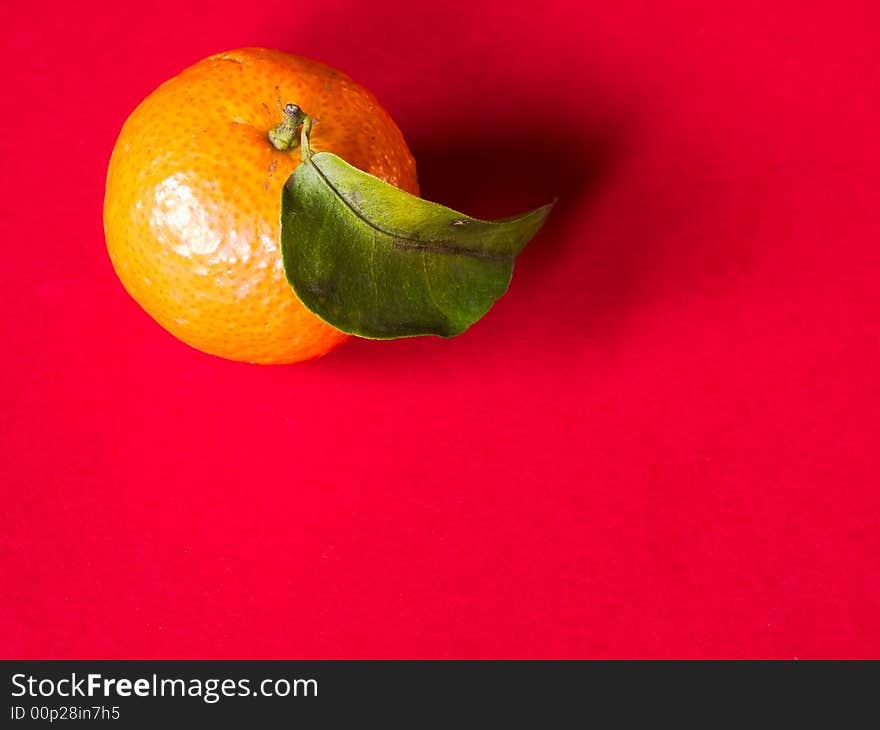 Still life of a single small tangerine with a leaf on red background illuminated from the side by the morning sun. Still life of a single small tangerine with a leaf on red background illuminated from the side by the morning sun