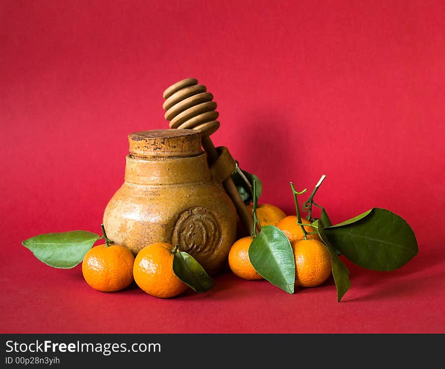 Still life of a hone pot with dipper and tangerines with leaves on red background illuminated by the morning sun from the side. Still life of a hone pot with dipper and tangerines with leaves on red background illuminated by the morning sun from the side