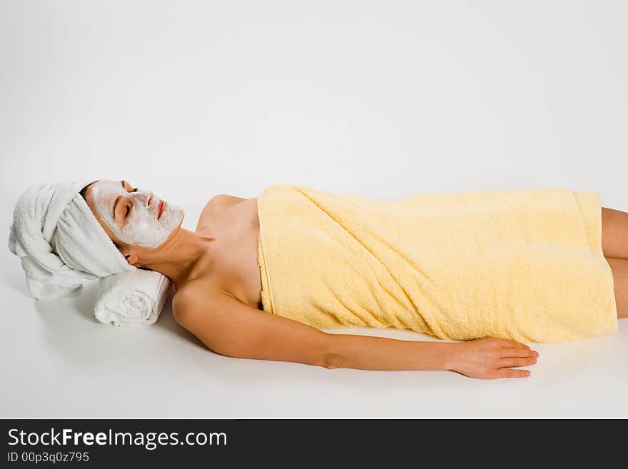 Woman in towels and facemask lying on white background. Woman in towels and facemask lying on white background.