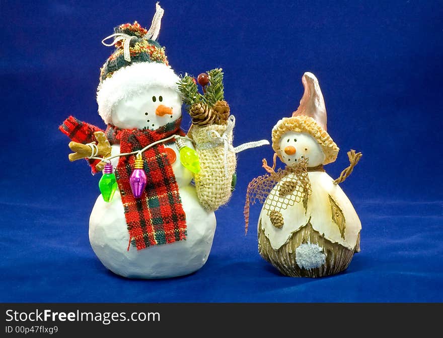 Two colorfully toy snowmen wearing Christmas decorations, isolated on a blue background. Two colorfully toy snowmen wearing Christmas decorations, isolated on a blue background.