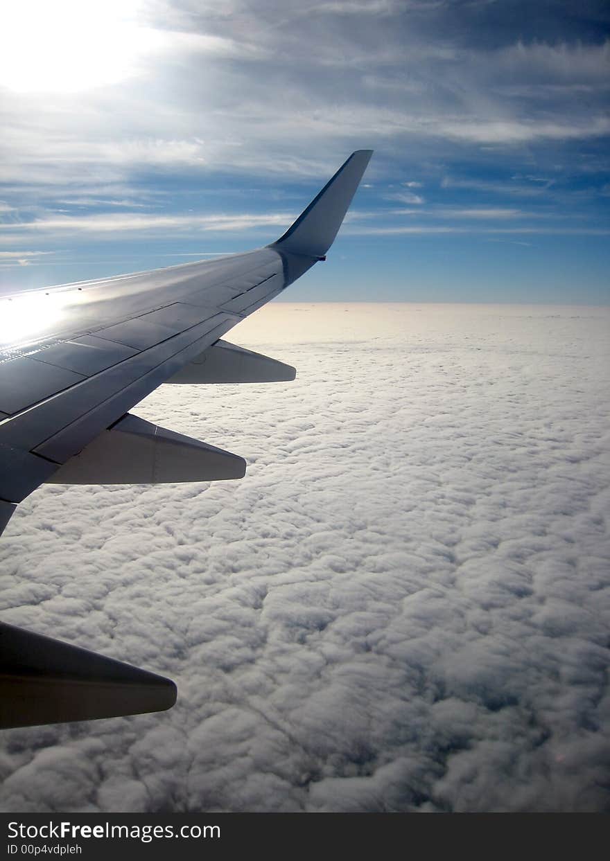 View from aircraft window showing wing and clouds below. View from aircraft window showing wing and clouds below