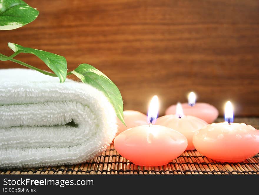 White towel, pink candle, green leaf in front of wood background. White towel, pink candle, green leaf in front of wood background